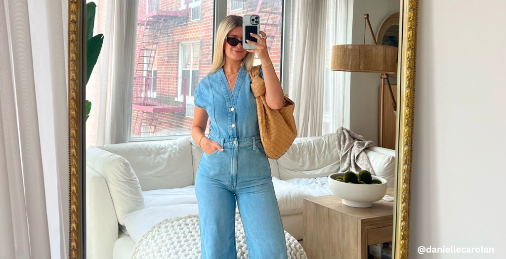 Creator @daniellecarolan takes a mirror selfie in a light denim jumpsuit with a tan woven tote bag and sunglasses, standing in a bright, modern living room.