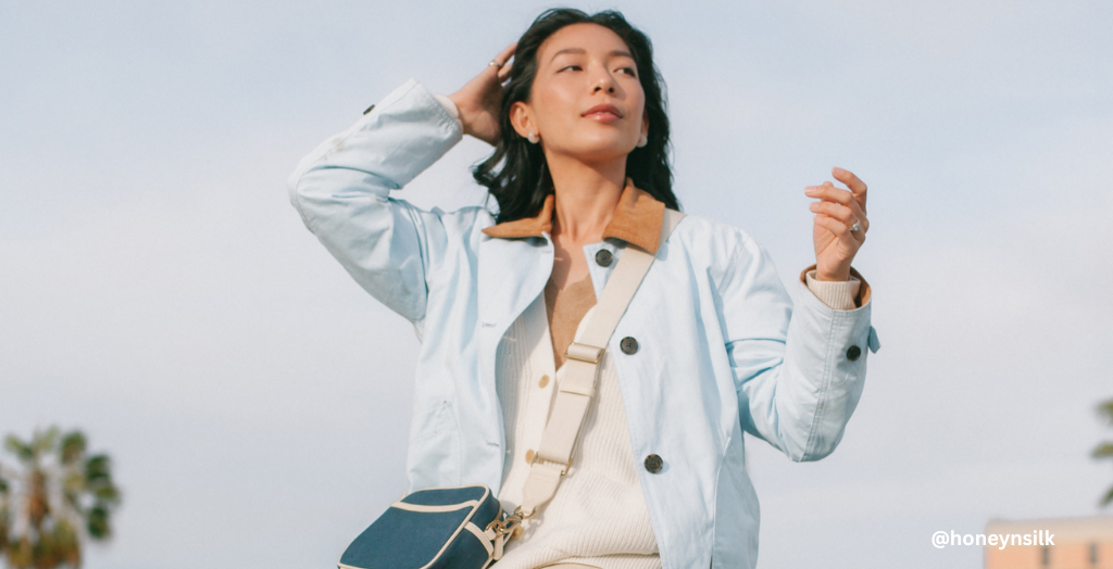 A Creator wearing a light blue coat with a tan strapped satchel against a blue sky backdrop