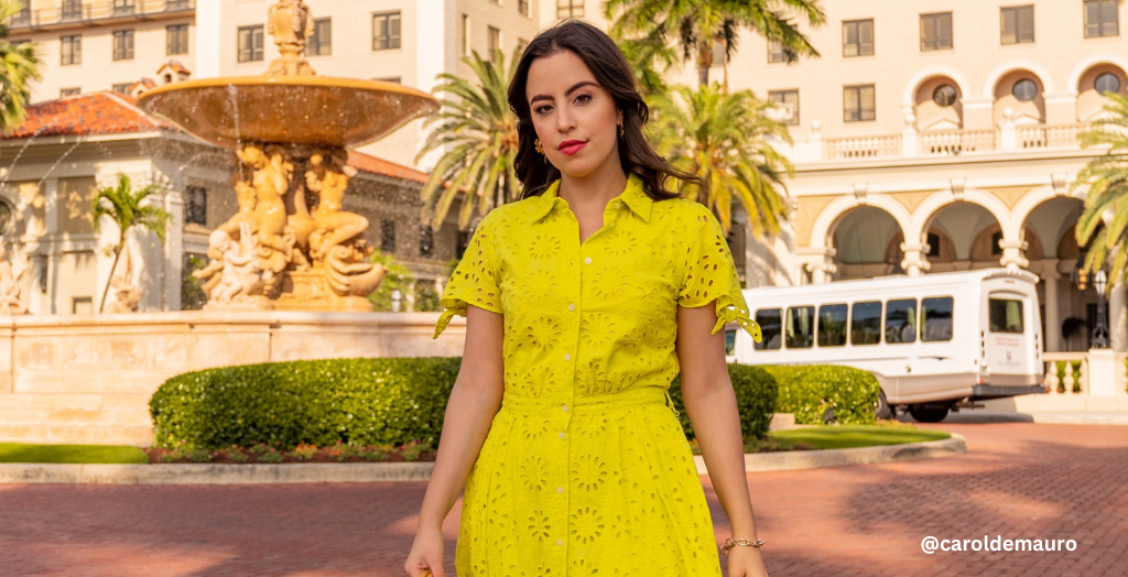 Creator @caroldemauro posing in front of a resort wearing a chartreuse dress with a floral pattern